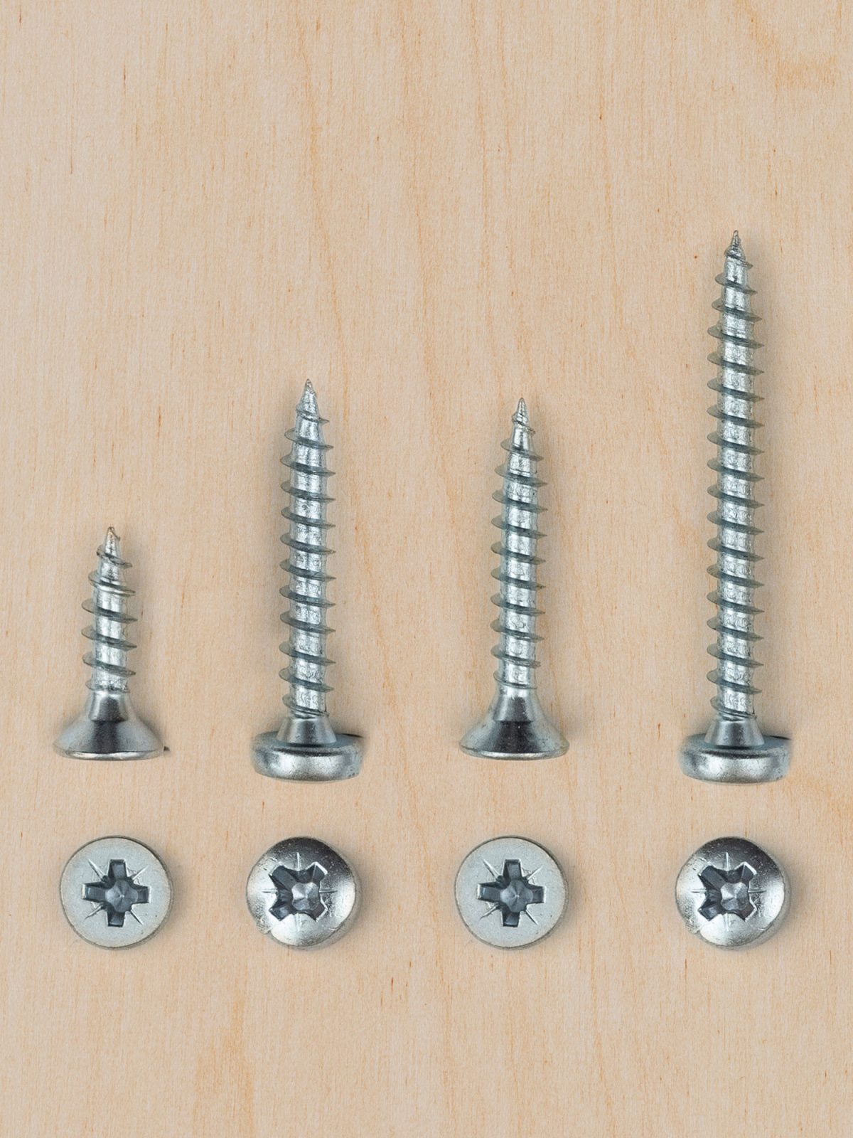 Screws of different sizes are laid out on a piece of wood, above four screws already inserted.