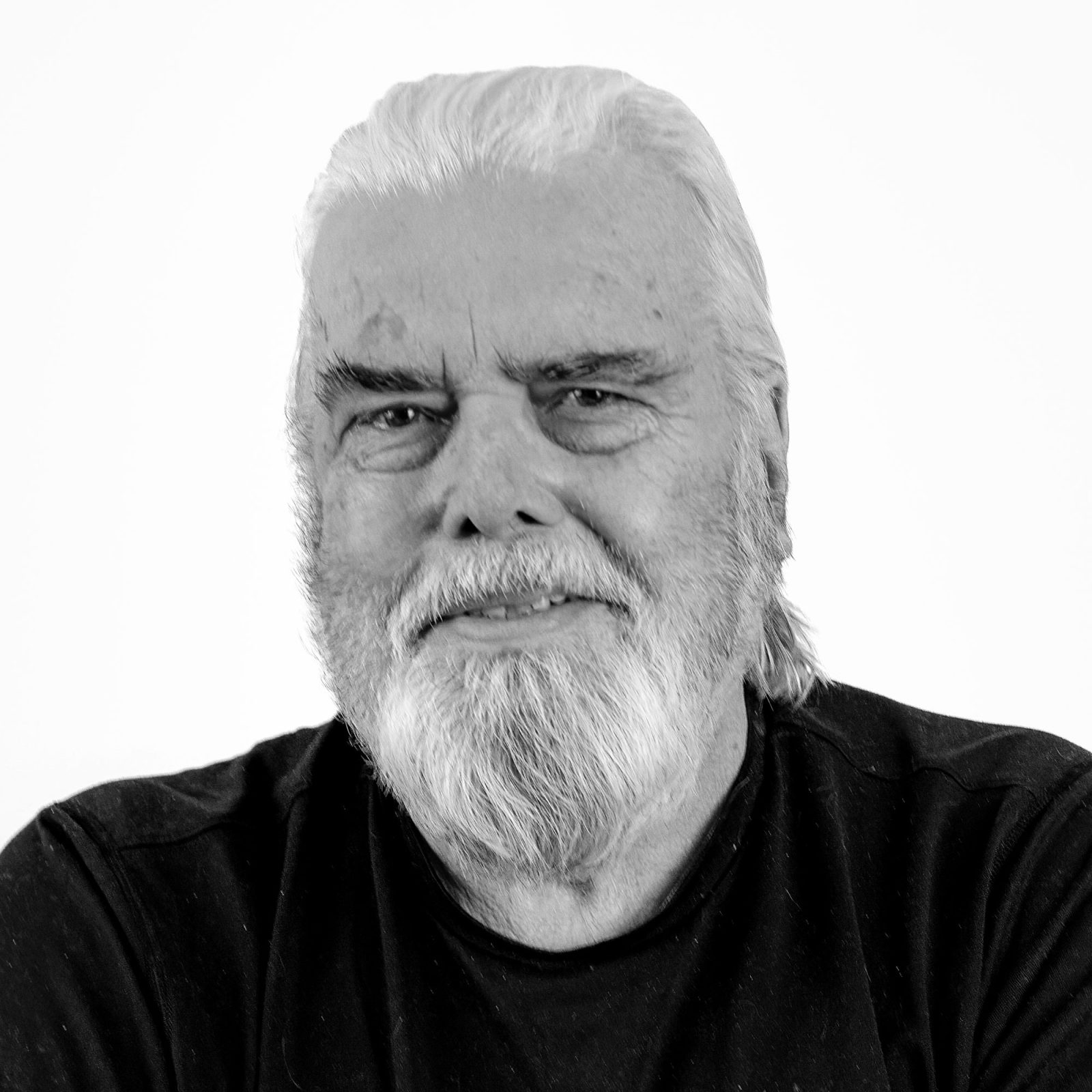 Vithårig äldre man, Hans Merving, med gråsprängt skägg och svart tröja.