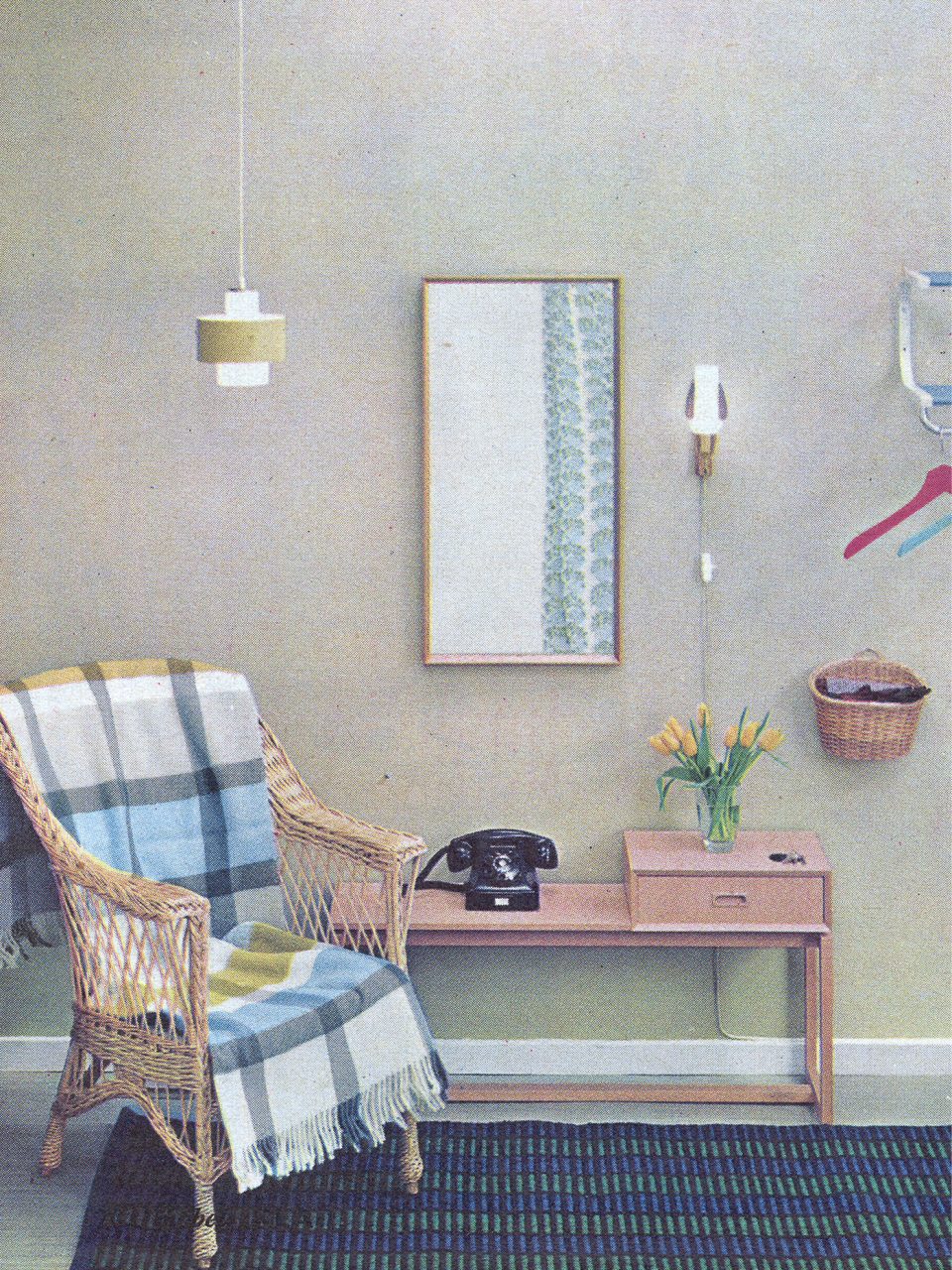 Black old telephone sits on TOSCA hall table in light wood. Over table is a hall mirror, next to it a wicker chair.