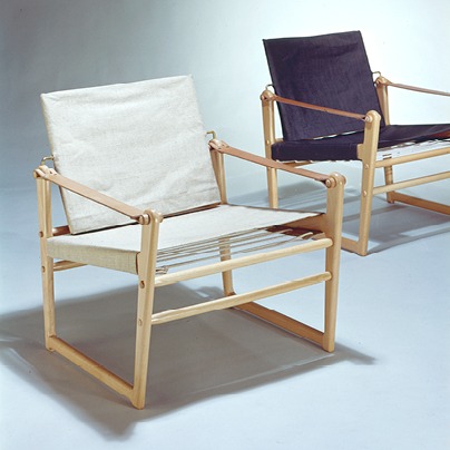 Two safari style armchairs, one black, one beige, with blond wood frames.