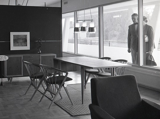 Young couple look at a 1950s room setting through a shop window.
