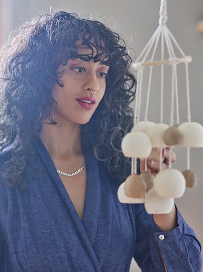 Mörkhårig kvinna i blå skjorta, Akanksha Deo, studerar en hängande mobil med vita och beige bollar.