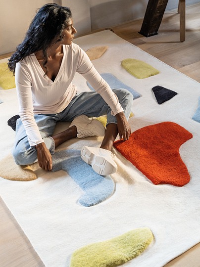 Mörkhårig kvinna i vit tröja sitter på en stor matta med 3D-mönster i olika skalor och färger.