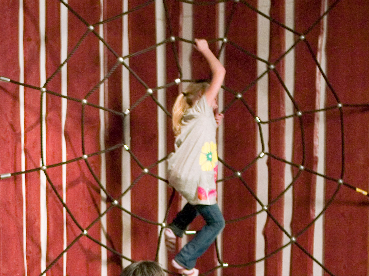 A child climbing a large spider net made of rope in a play area.