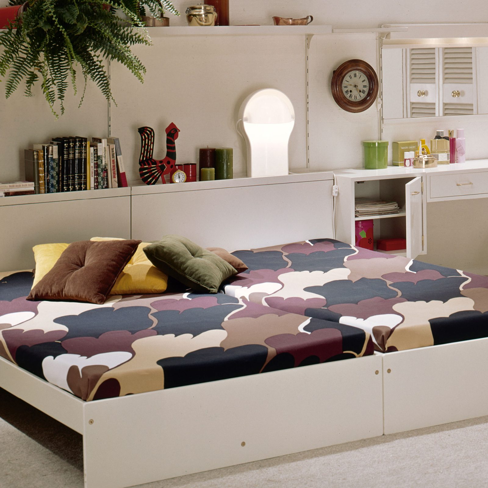 Sovrum i 1970-talsstil, en vit låg dubbelsäng med överkast i tassliknande mönster i brunt, svart och beige.