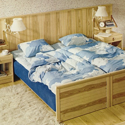 Sovrum i 1970-talsstil, furusäng bäddad med lakan med molnmönster.