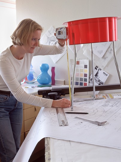 Blonde woman working in studio with a red side table and measuring tape.