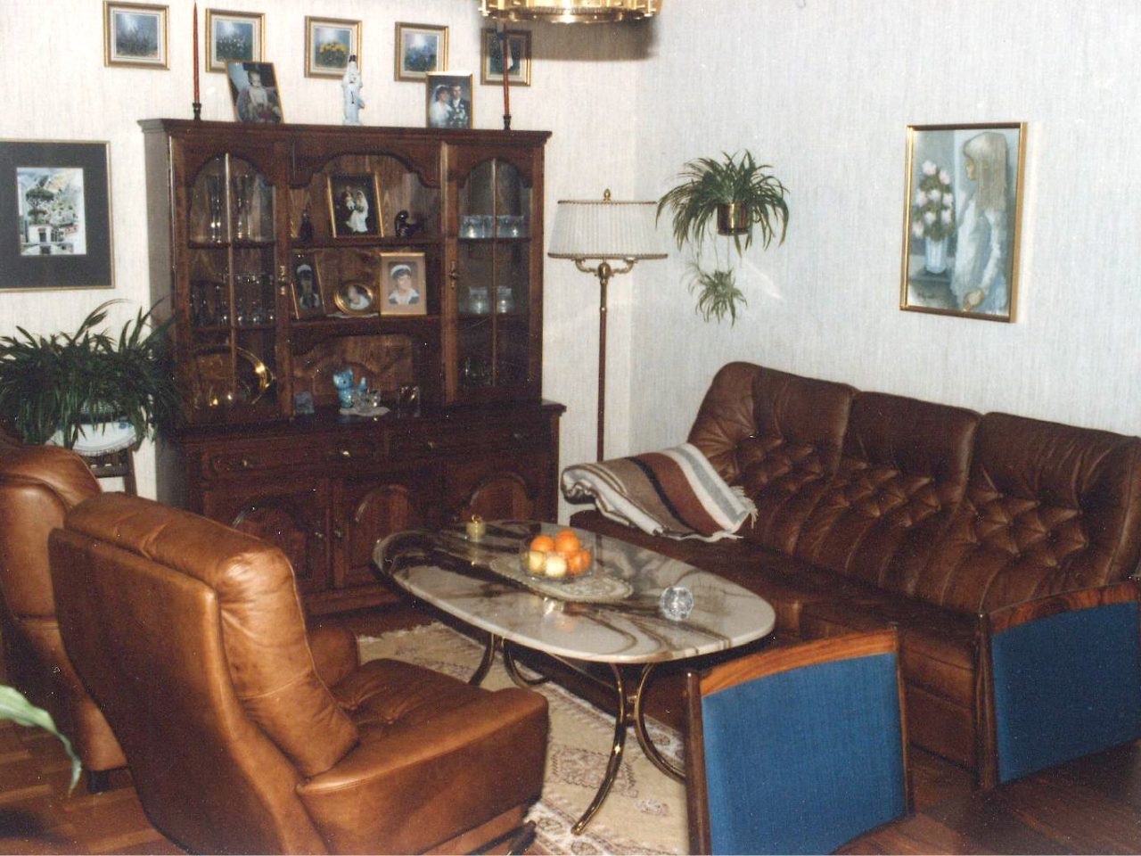 Vardagsrum i 1980-talsstil med skinnmöbler och vitrinskåp samt liten kristallkrona.