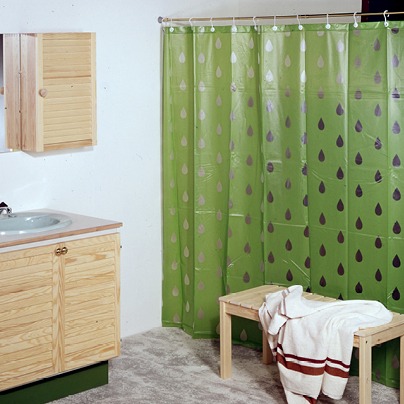 Badrum från 1970-talet med furuinredning och ett grönt duschdraperi med stora, genomskinliga droppar.