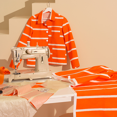 En jacka på en galge, en symaskin och tyglängd med orange och vita ränder.