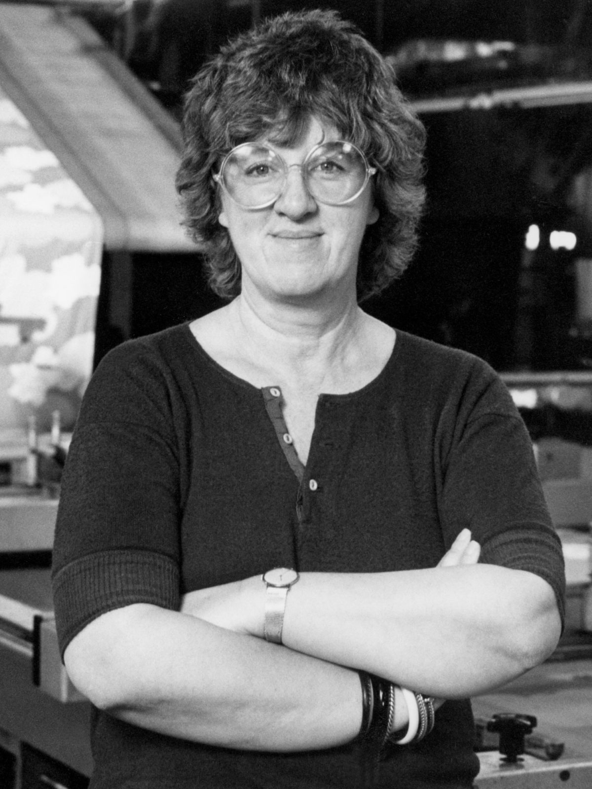 Kvinna med lockigt mörkt hår och runda glasögon med armarna i kors.