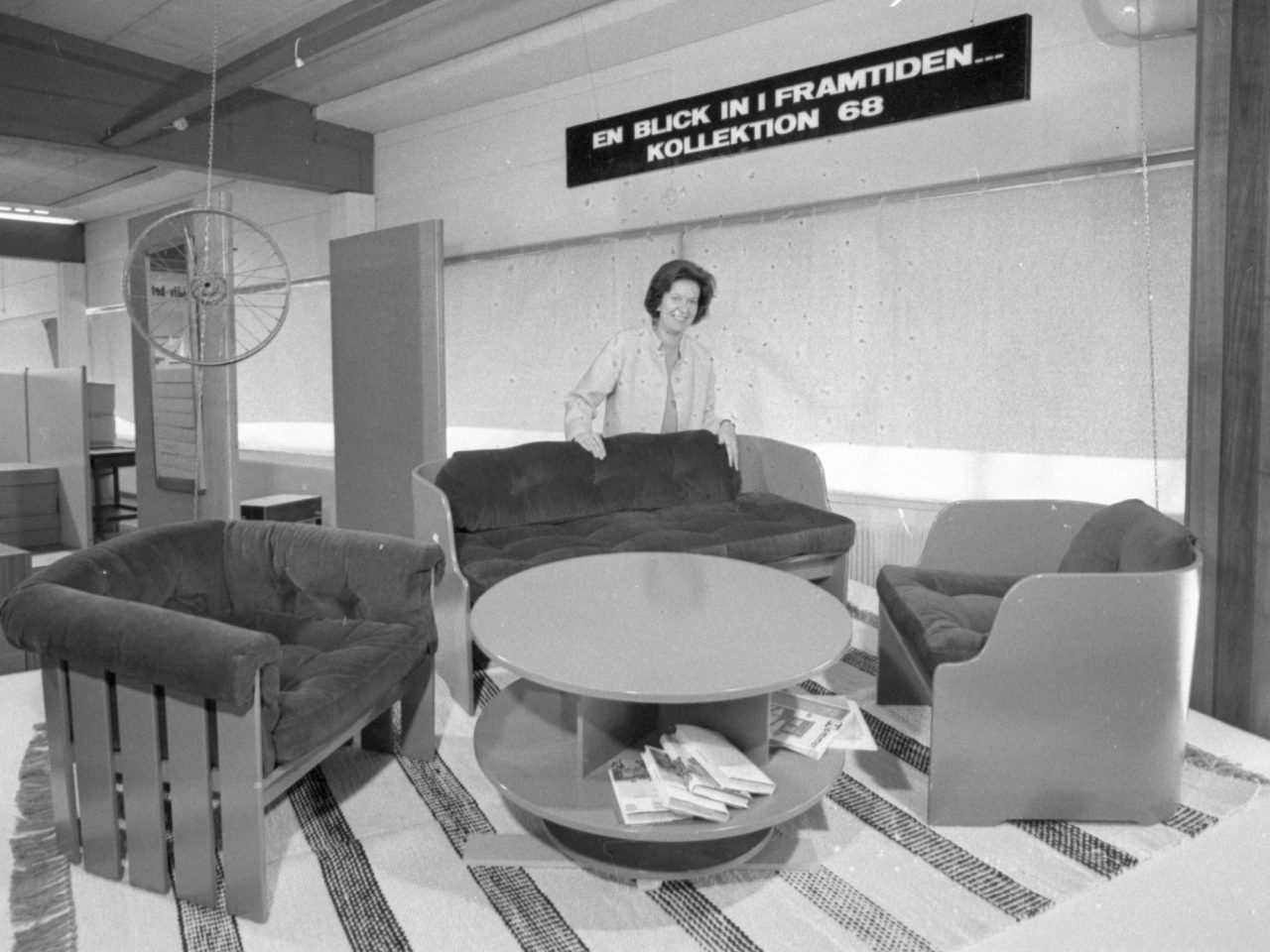 Dark-haired woman presenting comfortable chairs and a round table in a showroom.