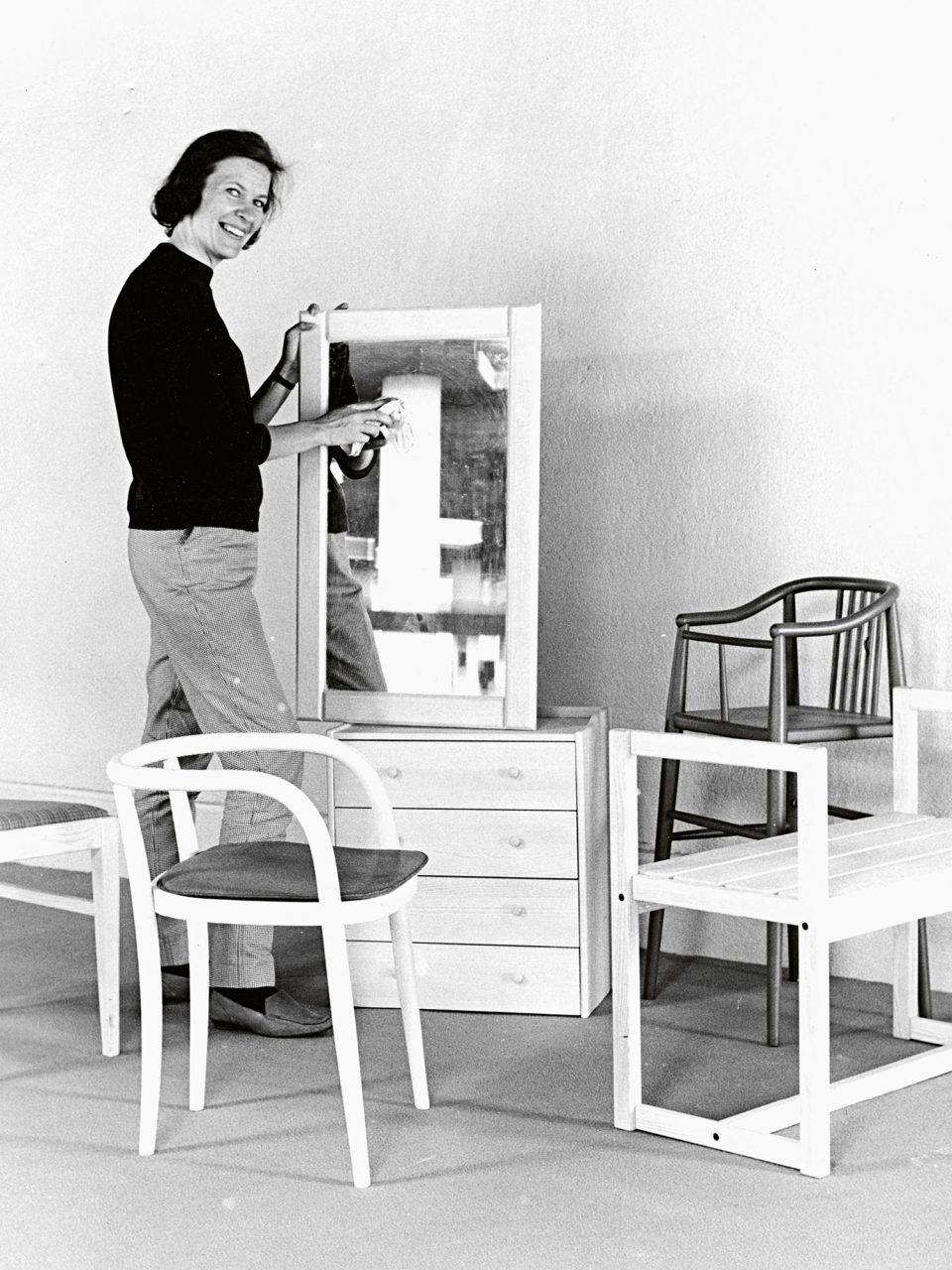 Woman in black sweater and slacks surrounded by pieces of furniture.