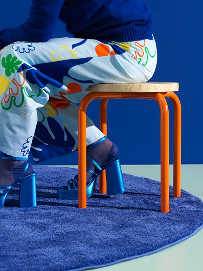 Stool with wooden seat and orange metal legs.