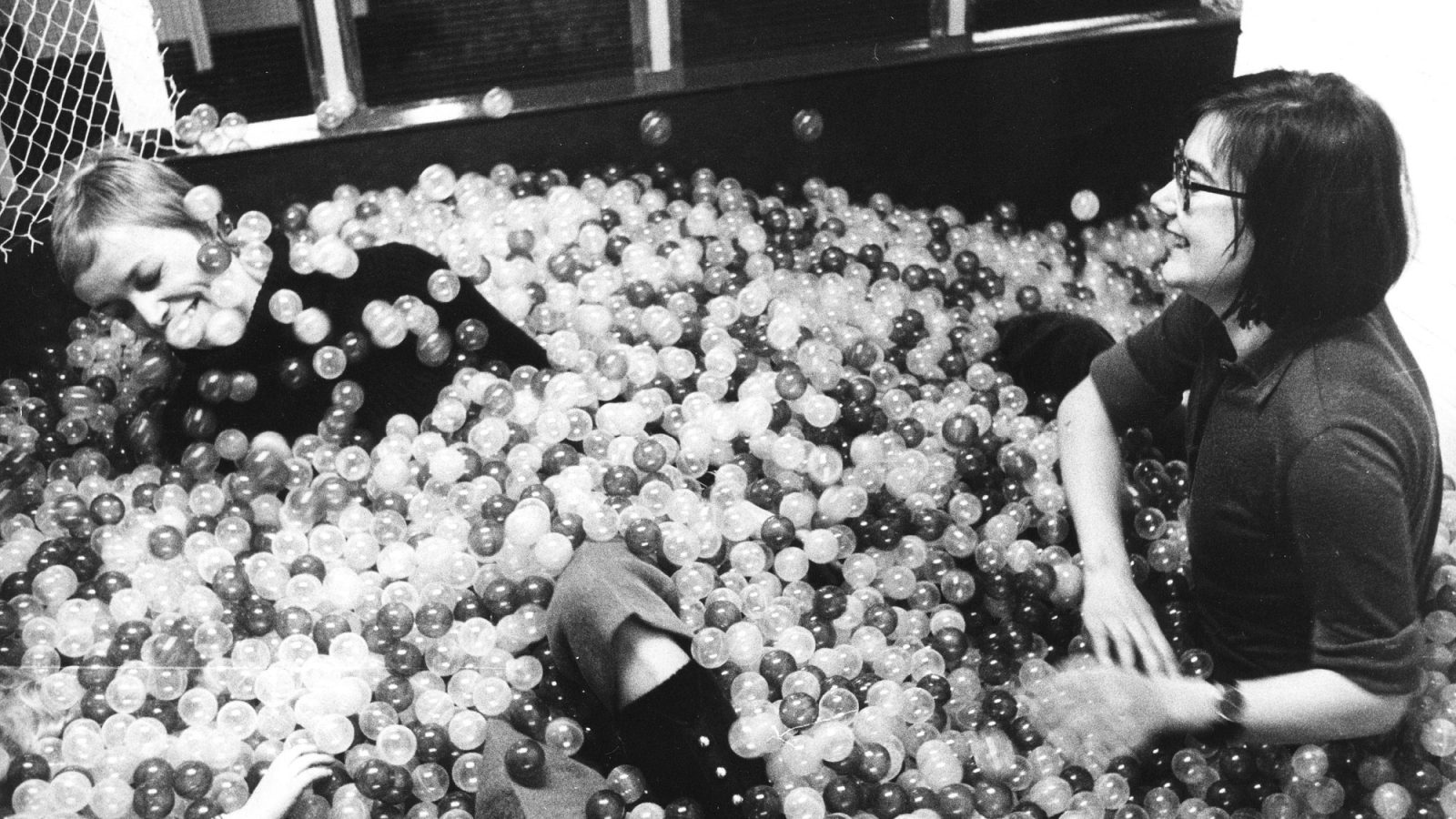 Två unga kvinnor leker i ett stort bollhav.