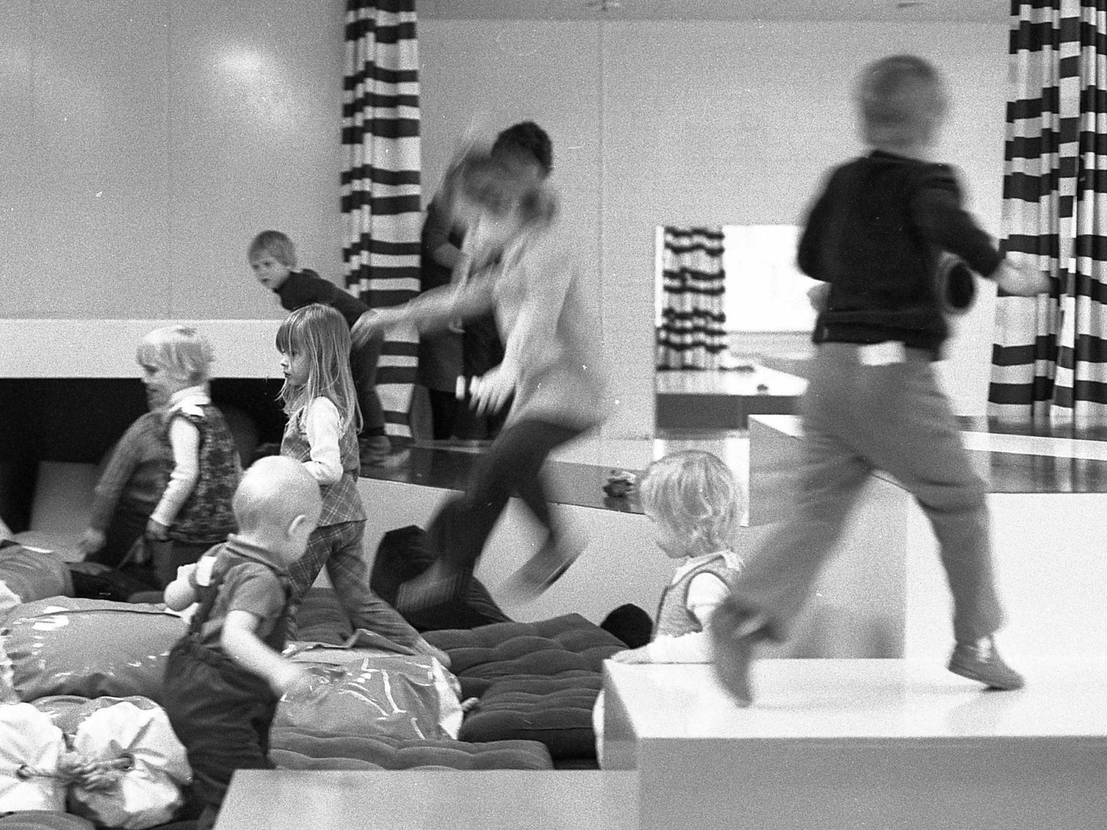 Barn hoppar och leker i ett stort lekrum med mjuka kuddar.