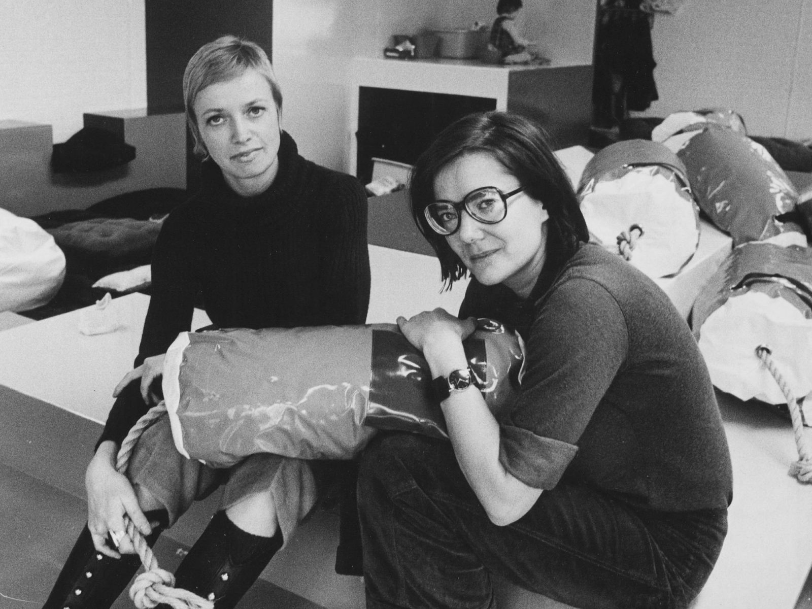 Två unga kvinnor sitter i ett stort lekrum, den ena håller i en mjuk avlång kudde.