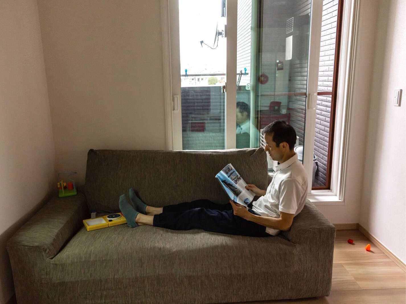 Man med japanskt utseende halvligger i liten brun soffa och läser tidningen.
