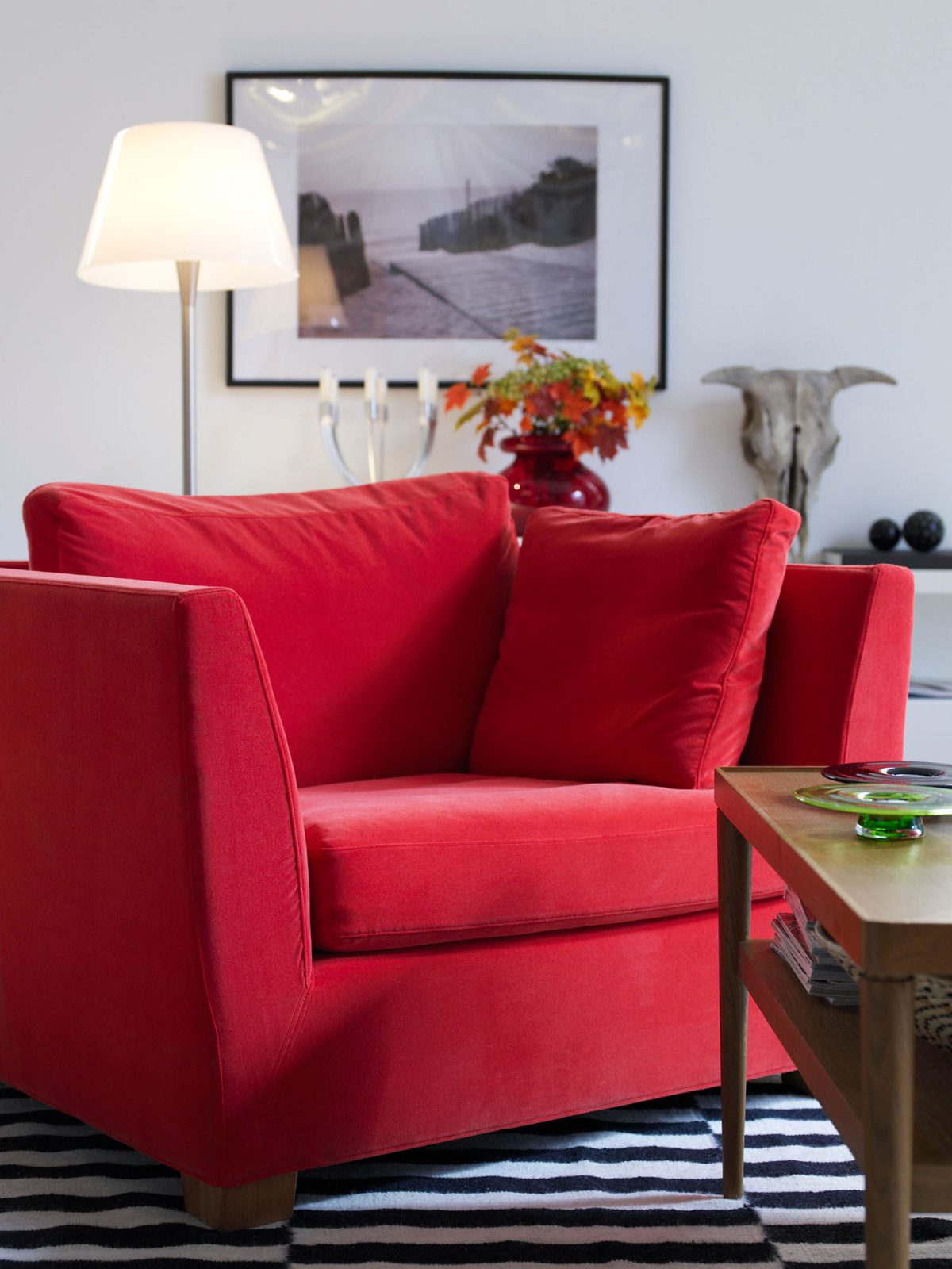 Bred röd fåtölj står på randig matta.