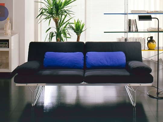 Enkel soffa med underrede av stålnät, svarta och blå kuddar.