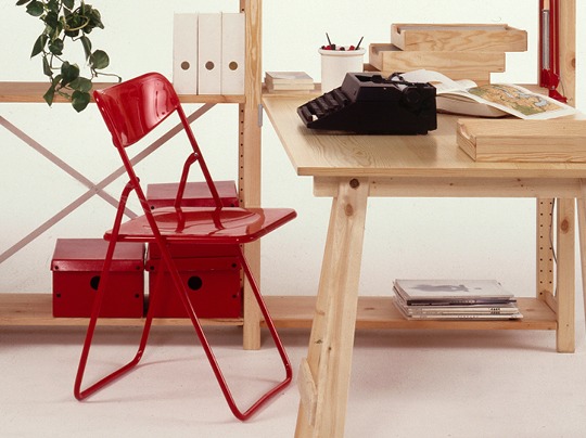 Röd fällstol står vid skrivbord i ljust trä.
