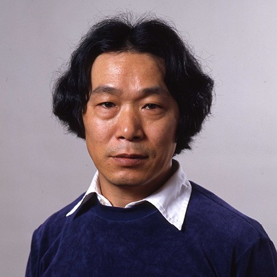 Japanese man with black hair, white shirt and blue sweater.