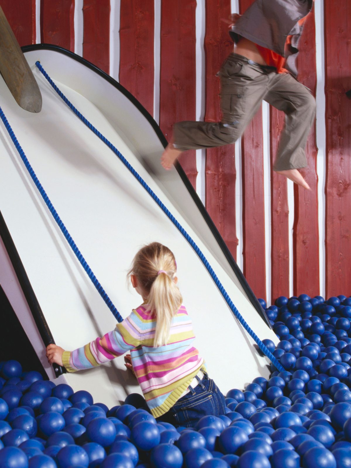 Barn leker i en vit rutschkana och ett bollhav med blåa plastbollar.