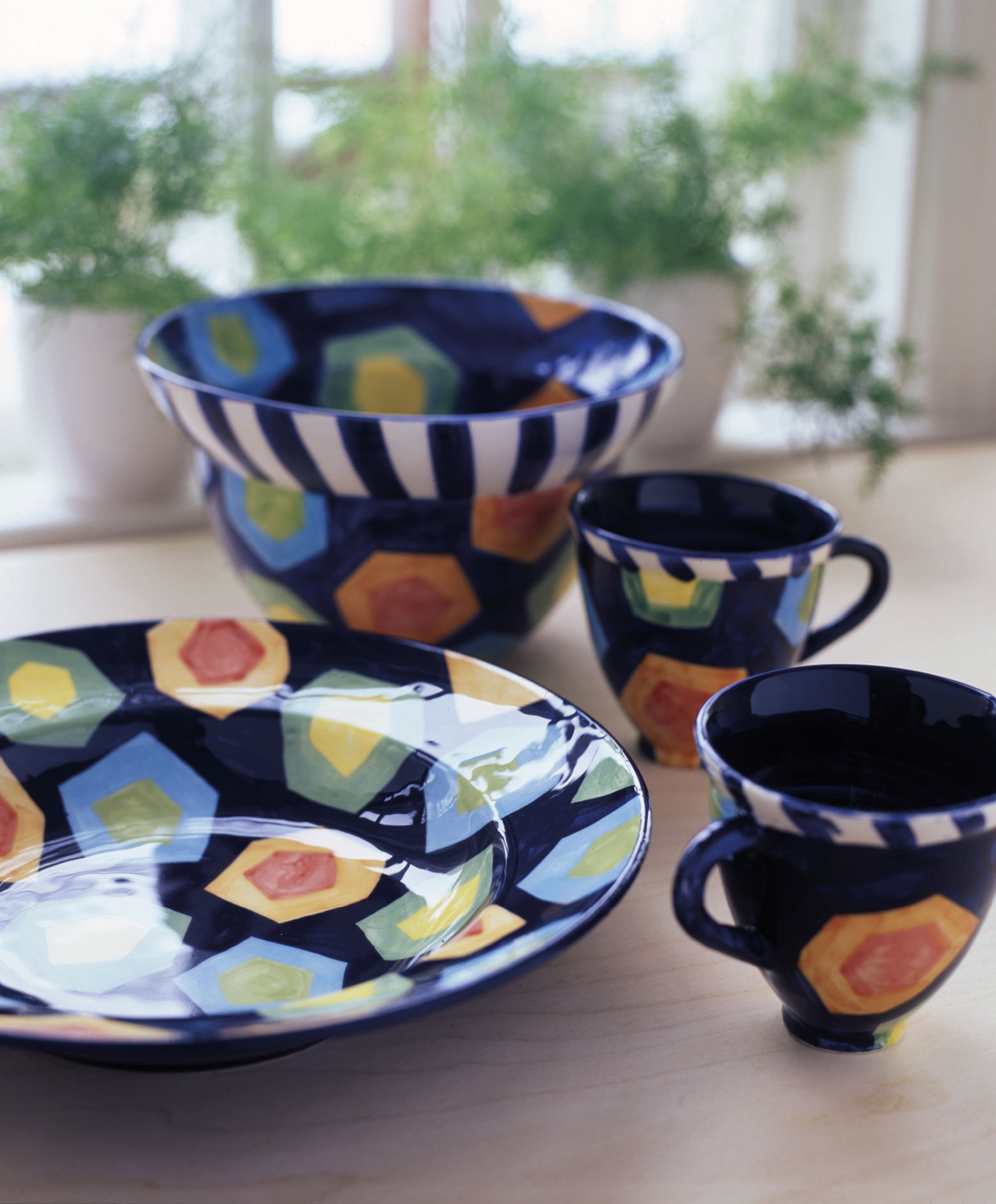 Colourful, expressive ceramic objects – plate, bowl and mugs on a windowsill.