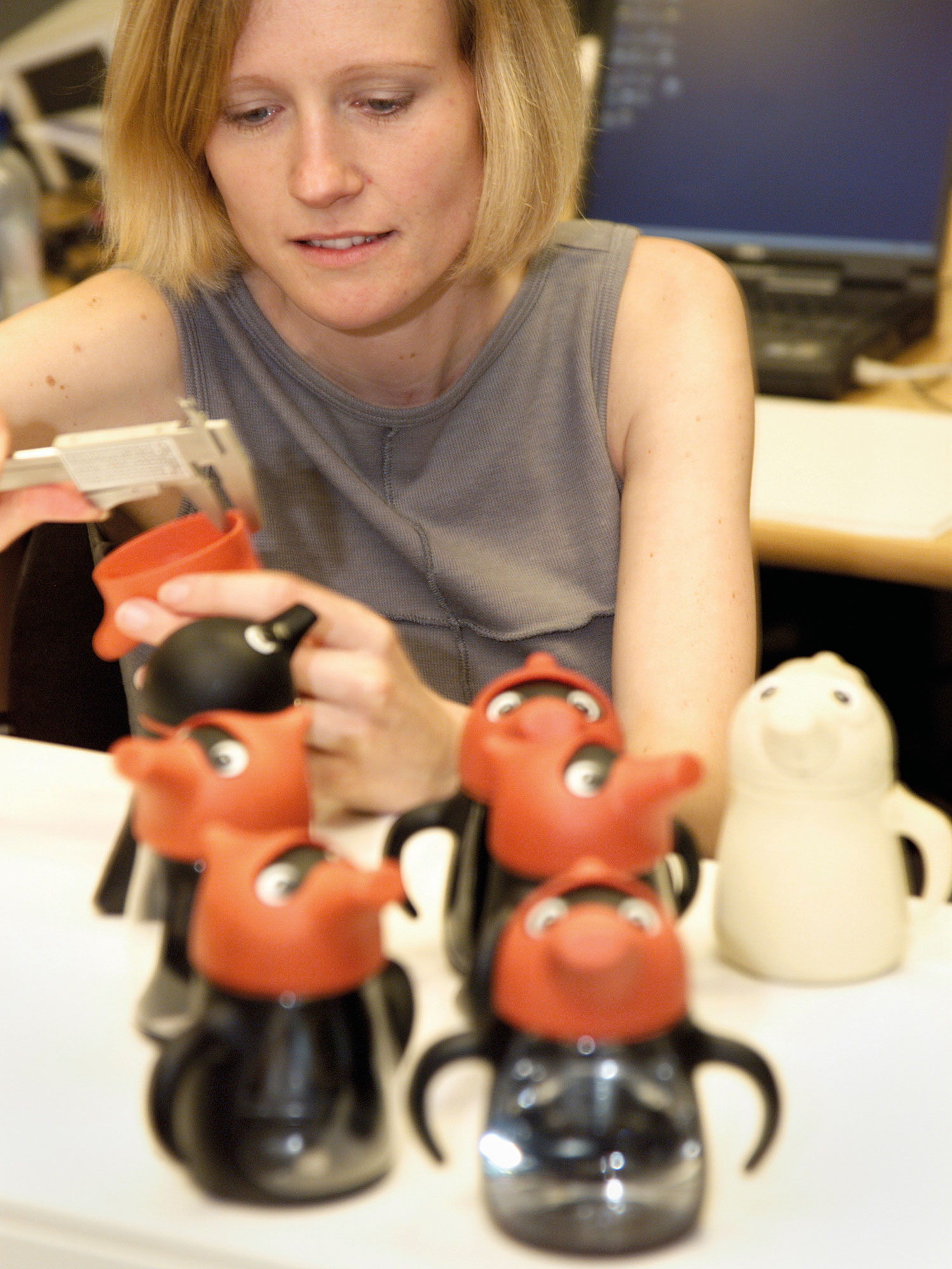 Blonde woman sitting behind toddler's plastic mugs shaped like quirky characters, and one beige prototype.