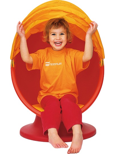 Ett leende barn som sitter i en röd snurrstol med orange huva, IKEA PS LÖMSK.