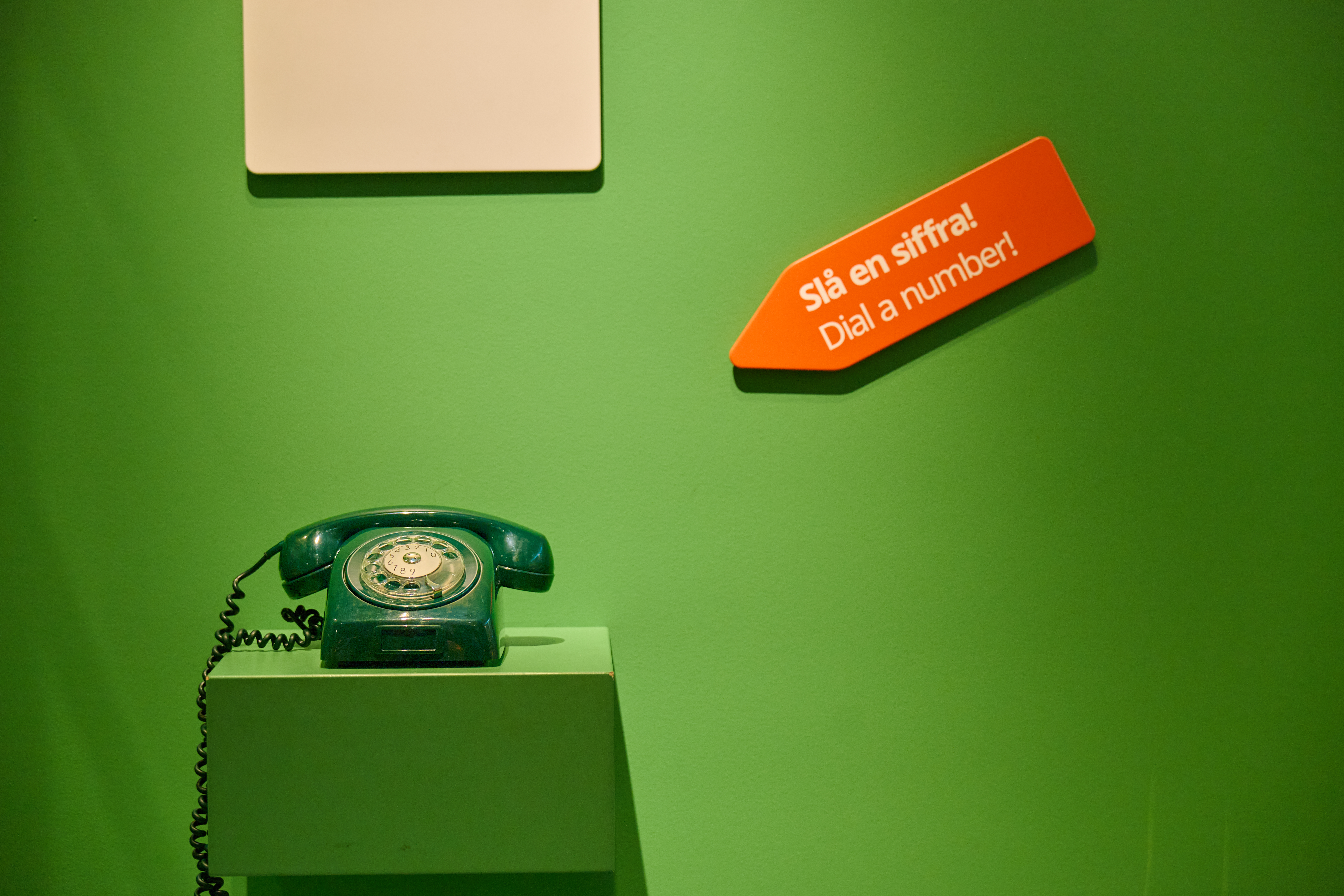A green vintage desk telephone on a green background that is part of the exhibition.