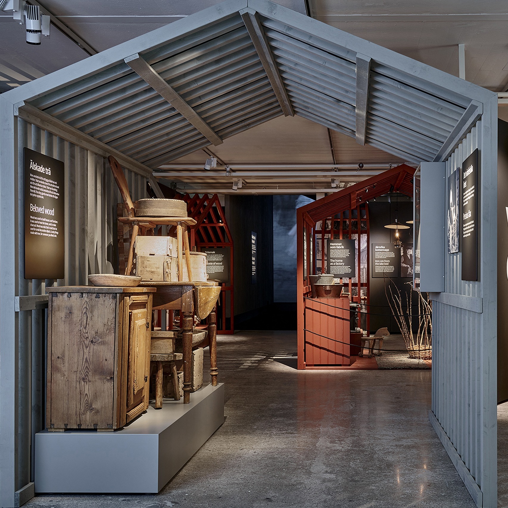 Exhibition walkway designed as a farm setting with historical tools, furniture, and red wooden structures.
